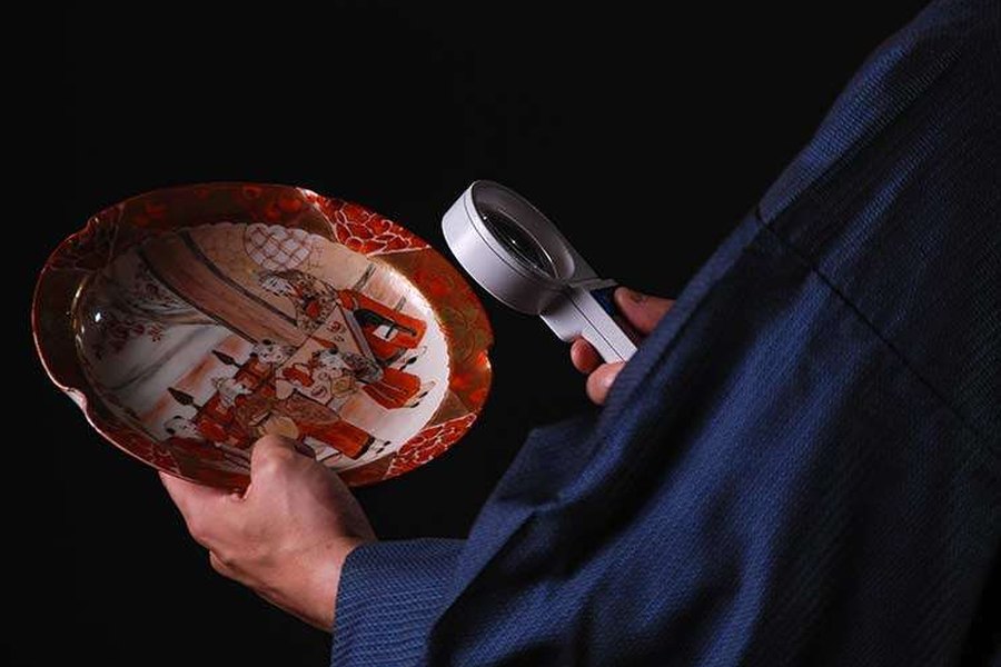 A valuer inspecting porcelain with a magnifying glass